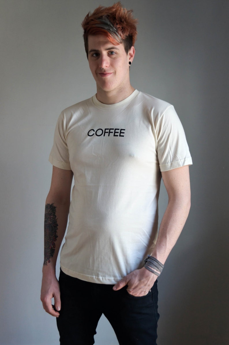 Light coloured, short sleeve t-shirt screen printed to say Coffee in dark font, modelled with dark pants.