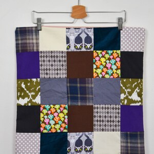 Peut inclure: Un oreiller patchwork avec une variété de motifs, y compris des chats, des champignons et des motifs géométriques. L'oreiller est suspendu à un cintre avec le numéro "#7" écrit sur un fond blanc.