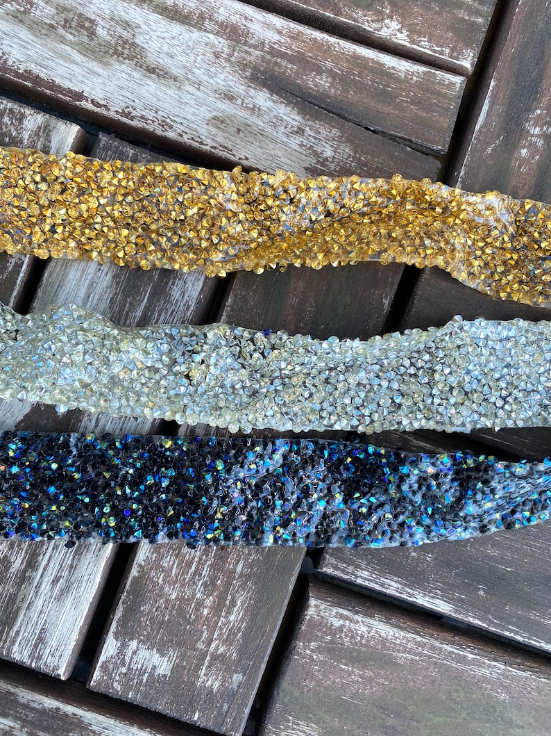 May include: Three strips of rhinestone trim in gold, clear, and iridescent black. The trim is made of small, faceted rhinestones.