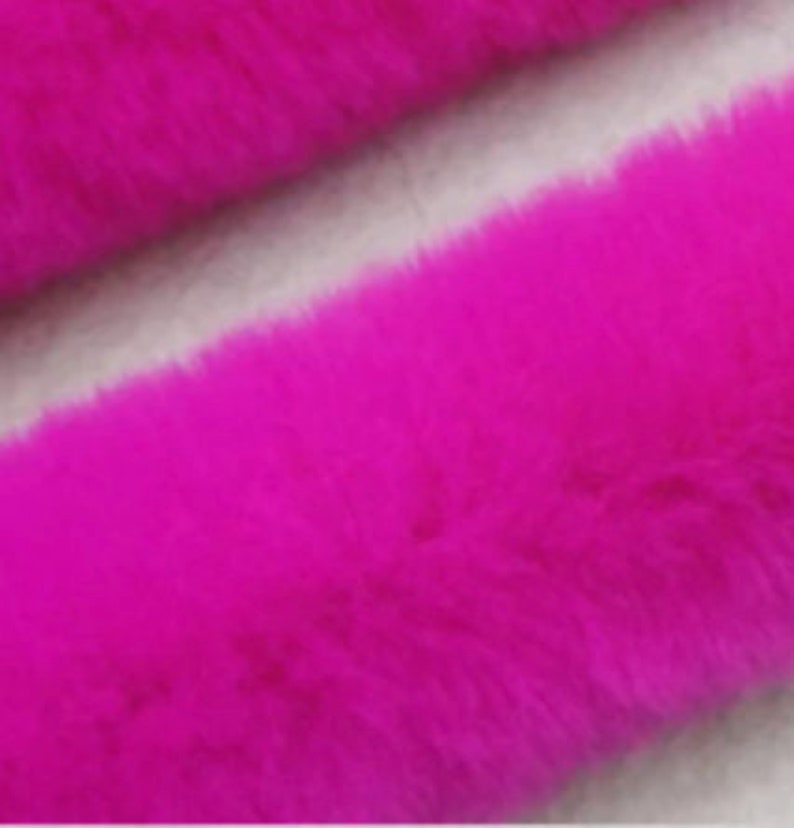 May include: A close-up of a bright pink faux fur fabric. The fabric has a soft, fluffy texture.