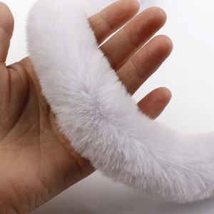 May include: A white faux fur trim, shown in a hand, is soft and fluffy. This trim is perfect for adding a touch of luxury to clothing, accessories, and home decor projects.
