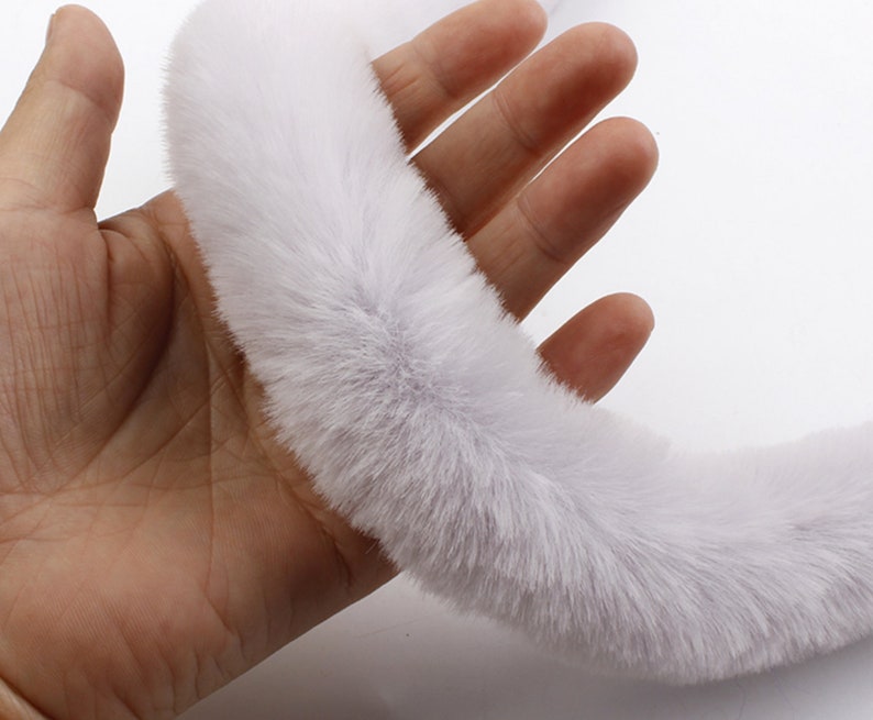 May include: A white faux fur trim, shown in a hand, is soft and fluffy. This trim is perfect for adding a touch of luxury to clothing, accessories, and home decor projects.