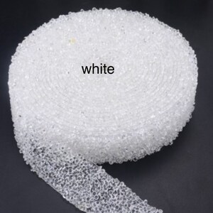 May include: White beaded trim, a close-up of a roll of white beaded trim. The trim is made of small, round beads that are sewn together.