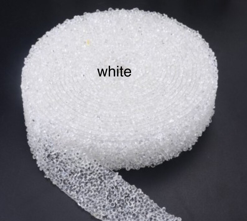 May include: White beaded trim, a close-up of a roll of white beaded trim. The trim is made of small, round beads that are sewn together.