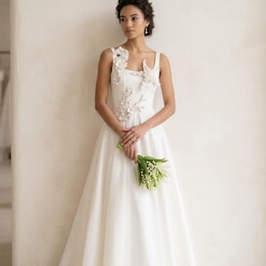 A model in a white bridal gown embellished with pearl seahorse, starfish, and coral appliques. A luxury white wedding dress with coastal themed pearl appliques on the bodice and shoulder.