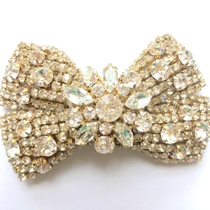 May include: A gold-toned bow brooch with a large, clear rhinestone center and smaller rhinestones surrounding it.