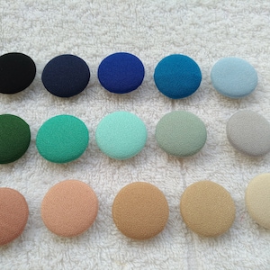 May include: Assortment of 15 round fabric buttons in various colors, including black, navy blue, teal, light blue, gray, green, mint green, beige, and peach.