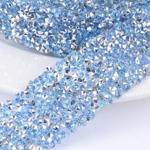 May include: A roll of light blue rhinestone trim with a silver backing. The trim is made of small, faceted rhinestones that are closely spaced together.