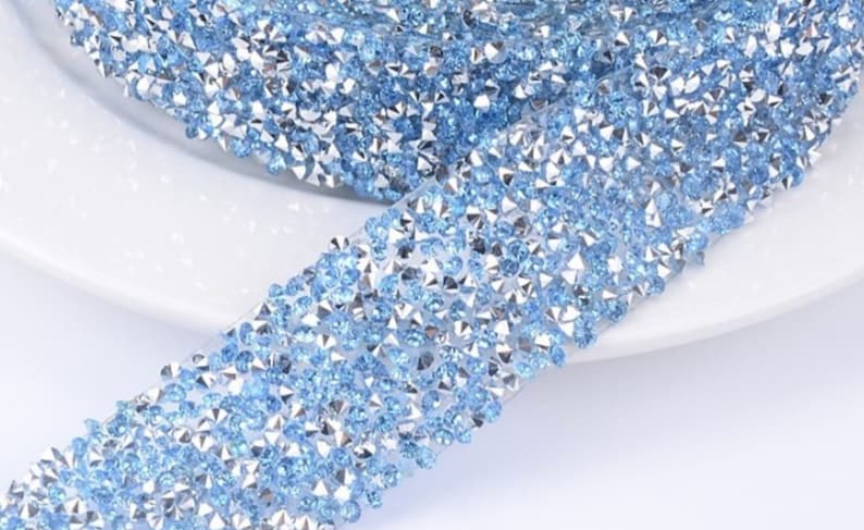 May include: A roll of light blue rhinestone trim with a silver backing. The trim is made of small, faceted rhinestones that are closely spaced together.