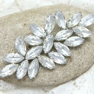 Peut inclure: Un groupe de strass en cristal transparent disposés en motif floral. Les strass sont sertis dans du métal argenté.