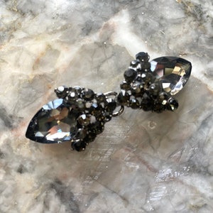 May include: A pair of black crystal teardrop-shaped embellishments with a metal connector in the centre.
