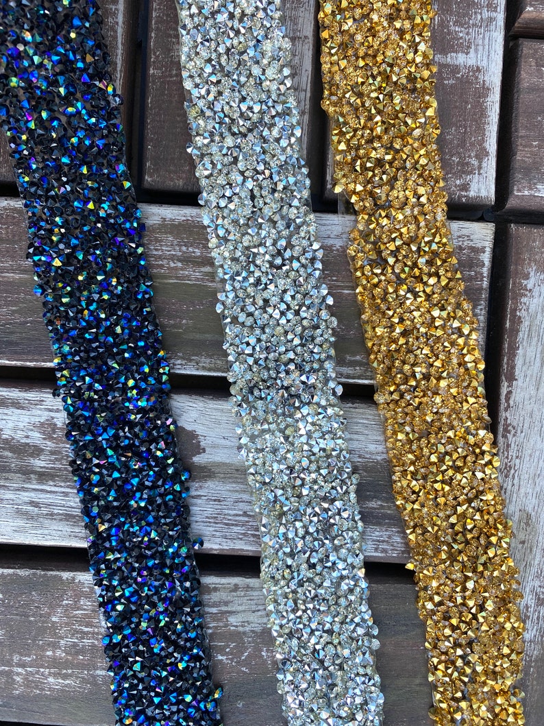 May include: Three strips of rhinestone trim in blue, silver, and gold. The trim is made of small, faceted rhinestones that are sewn onto a clear backing.