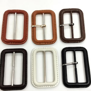 Pode incluir: Seis fivelas retangulares para cinto em várias cores: castanho, bege, castanho escuro, branco e preto. Cada fivela tem uma barra de metal prateado e uma moldura de couro ou semelhante.