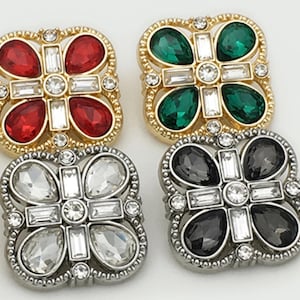 以下が含まれることがあります： 四つの装飾的な正方形のボタン。それぞれ金または銀色の金属フレームで、中央に十字のデザインがあります。ボタンは赤、緑、透明、黒の宝石で飾られています。