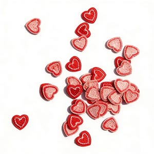 Puede incluir: Un conjunto de pequeños parches en forma de corazón, en tonos rojos y rosas, dispersos sobre un fondo blanco. Los parches tienen un borde cosido y los corazones están rellenos con un diseño texturizado. Ideales para manualidades y adornos.