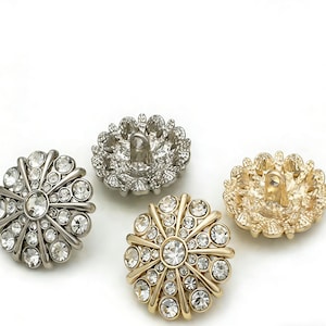 Può includere: Quattro bottoni decorativi in finiture argento, oro e argentate. Ogni bottone presenta un design floreale con strass trasparenti e scintillanti. I bottoni sono rotondi e hanno un anello sul retro per cucire.