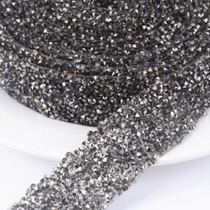 May include: A roll of black rhinestone trim with a shiny, sparkly finish. The trim is made of small, faceted rhinestones that are closely spaced together.