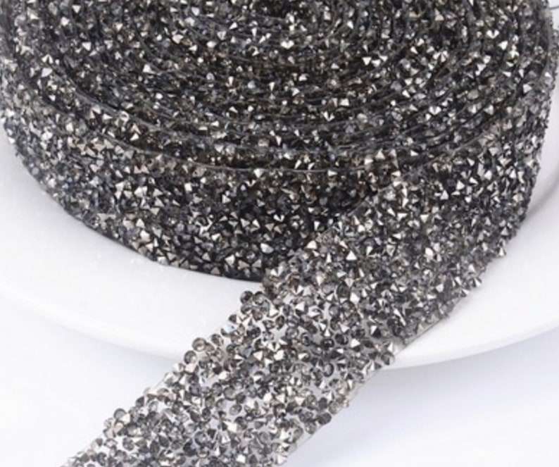 May include: A roll of black rhinestone trim with a shiny, sparkly finish. The trim is made of small, faceted rhinestones that are closely spaced together.
