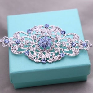 Op de afbeelding: Een zilveren filigraan broche met lichtblauwe strass steentjes. De broche heeft een delicaat, ingewikkeld ontwerp en is perfect om elke outfit een vleugje glans te geven.