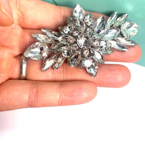 以下が含まれることがあります： 花のようなデザインのクリアなラインストーンのクラスターが付いた大きなシルバーのブローチ