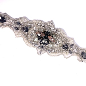 May include: A silver and black beaded embellishment with a floral design. The embellishment is made of pearls, rhinestones, and other decorative elements.