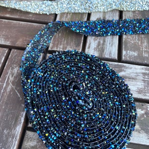 May include: A roll of black and blue iridescent rhinestone trim. The trim is made of small, faceted rhinestones that are sewn onto a clear, flexible backing.