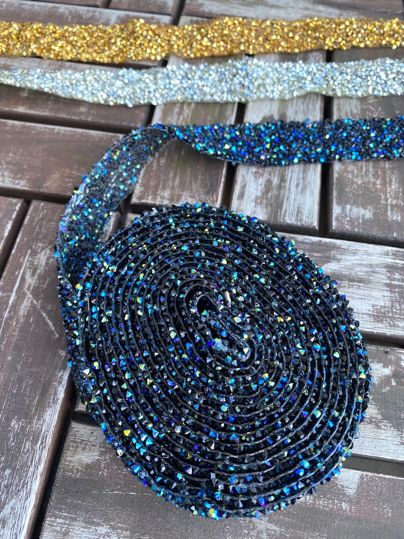 May include: A roll of black and blue iridescent rhinestone trim. The trim is made of small, faceted rhinestones that are sewn onto a clear, flexible backing.