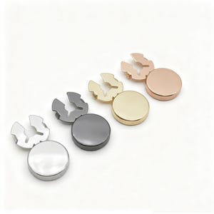 May include: A collection of metal snap fasteners in silver, gunmetal, gold, and rose gold. Each fastener consists of a round cap and a U-shaped spring clip. The fasteners are arranged on a white background.