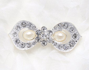May include: A silver bow-shaped brooch with clear rhinestones and two faux pearl accents.