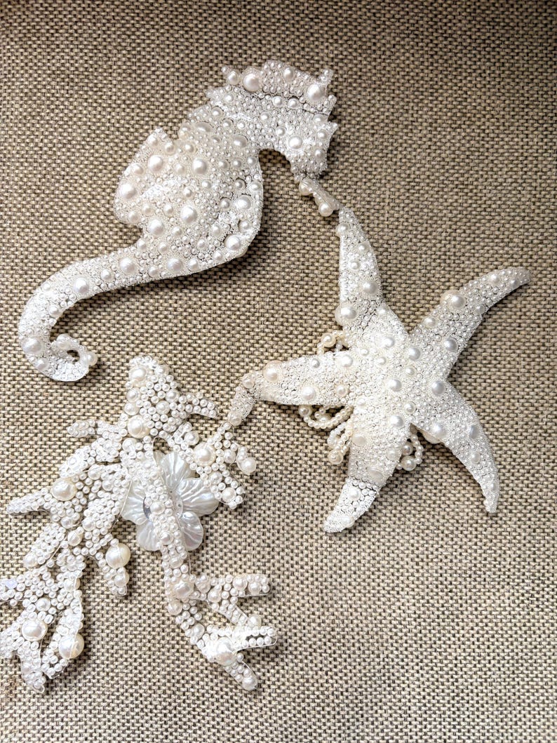 Close up view of a pearl seahorse applique featuring a delicate 3D white fabric flower.