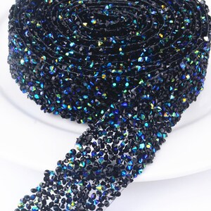 May include: A roll of black rhinestone trim with iridescent blue and green accents. The trim is made of small, faceted rhinestones that are sewn onto a clear mesh backing.