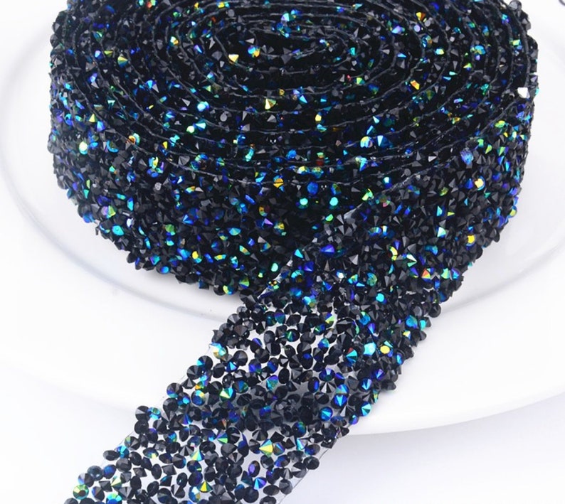 May include: A roll of black rhinestone trim with iridescent blue and green accents. The trim is made of small, faceted rhinestones that are sewn onto a clear mesh backing.