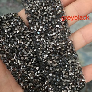 May include: Close-up of a roll of grey-black rhinestone trim. The trim is made of small, pointed rhinestones that are closely spaced together.