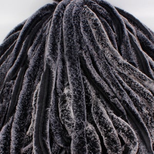 May include: A close-up of a dark gray faux fur fabric with a wavy, textured pattern. The fabric is soft and plush, and it would be ideal for making a variety of garments or home decor items.