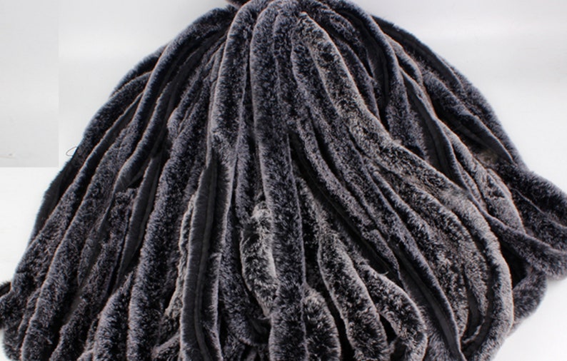 May include: A close-up of a dark gray faux fur fabric with a wavy, textured pattern. The fabric is soft and plush, and it would be ideal for making a variety of garments or home decor items.
