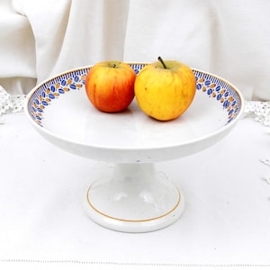 May include: A white ceramic cake stand with a blue and gold floral pattern around the edge. Two apples, one red and one yellow, are on the stand.
