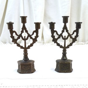 May include: Two antique bronze candle holders with ornate designs. Each holder has three candle arms and a hexagonal base.