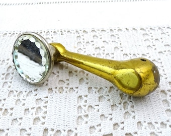 May include: A gold-toned metal handle with a round, faceted glass mirror on one end. The handle is shaped like a bird's head.