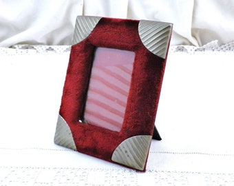 May include: A small, red velvet picture frame with silver corners. The frame has a stand on the back and is ready to display a photo.