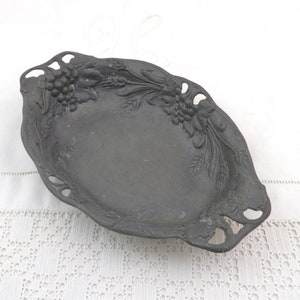 Könnte beinhalten: Eine schwarze Metall-Servierplatte mit Trauben- und Blattdesign. Die Platte hat zwei ausgeschnittene Griffe auf jeder Seite.
