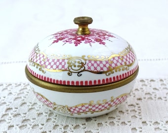 Könnte beinhalten: Eine kleine, runde, weiße Porzellan-Schmuckdose mit einem rosa-goldenen Blumendesign. Die Dose hat einen Messingdeckel mit einem Knopf.