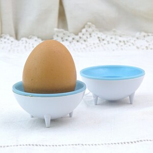 May include: A brown egg in a white and light blue egg cup with three legs. The egg cup is on a white tablecloth.