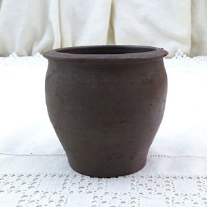 May include: A dark brown, unglazed, ceramic pot with a rounded body and a slightly flared rim.