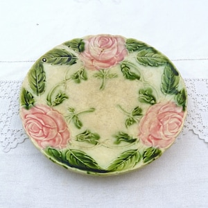 Puede incluir: Un plato de cerámica vintage con un diseño en relieve de rosas rosas y hojas verdes. El plato tiene un fondo crema.