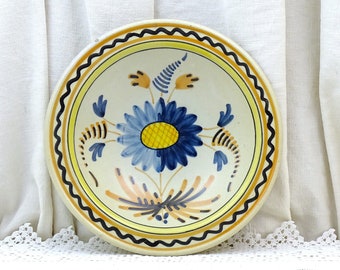 May include: A white ceramic bowl with a blue and yellow floral design. The bowl has a scalloped edge and a black rim.