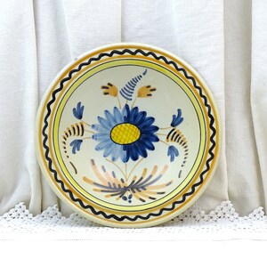 May include: A white ceramic bowl with a blue and yellow floral design. The bowl has a scalloped edge and a black rim.
