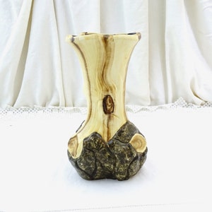 Könnte beinhalten: Eine Holzvase mit natürlicher Holzmaserung. Die Vase ist in Form eines Baumstamms gestaltet und hat eine braune und schwarze, rindenartige Textur.