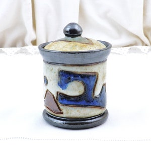 Può includere: Un vaso di ceramica con coperchio, con un design astratto blu, marrone e bianco. Il vaso ha una smaltatura grigio scuro.