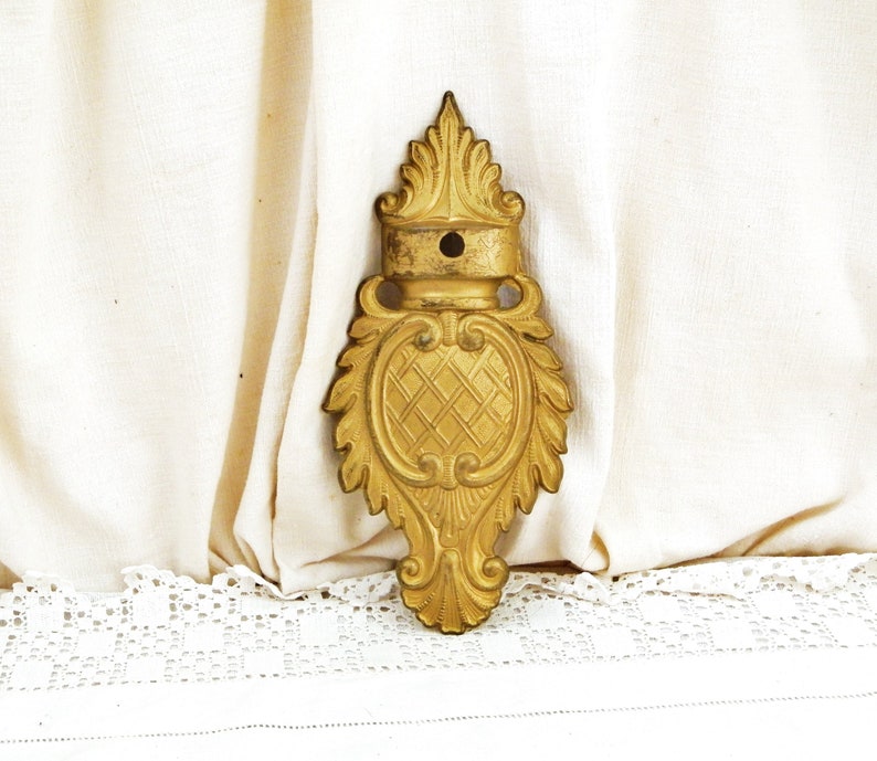 May include: A gold-colored metal decorative wall mount with a floral design. The mount has a small hole in the center.