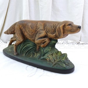 May include: A brown dog statue in a running pose, atop a green and black base with foliage details. The dog has a detailed fur texture and a focused expression. This decorative piece is suitable for home decor.